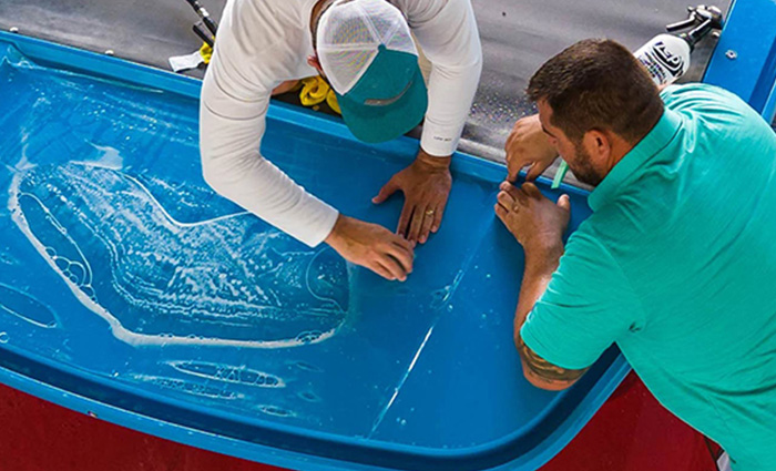 Aerial view of two adult males applying a protective film to blue boat panels.