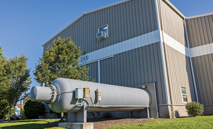 Exterior view of a large warehouse with silver siding and two green trees in front on a clear, sunny day.