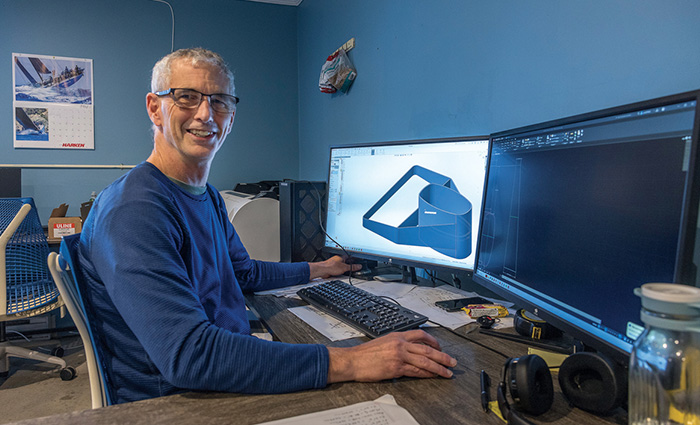 Middle-aged man with gray hair wearing eyeglasses and a long sleeve blue shirt sitting at a desk with dual monitors.