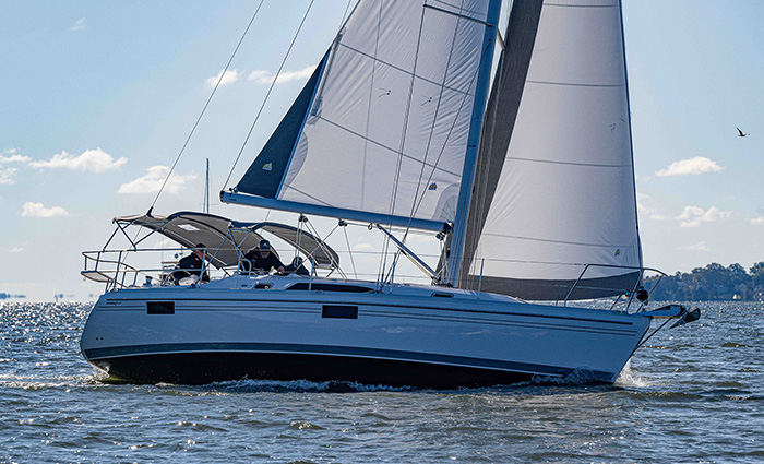 Three adult males aboard a white sailboat with blue trim out on open waters on a sunny day.
