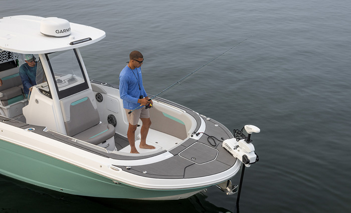 Adult male wearing a long sleeve blue shirt and tan shorts standing at the bow of a vessel out on the water. 