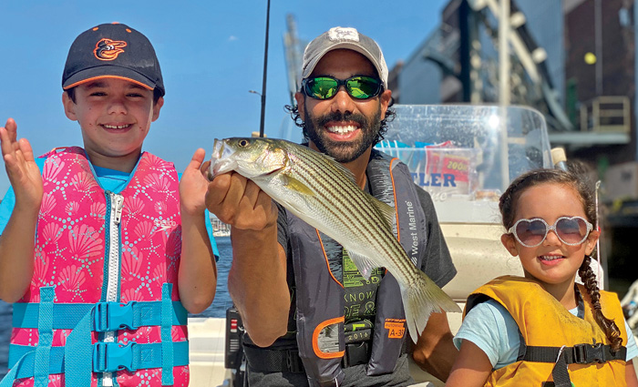 Bearded adult male proudly showing a fish caught with a young boy on the right and a young girl on the left.