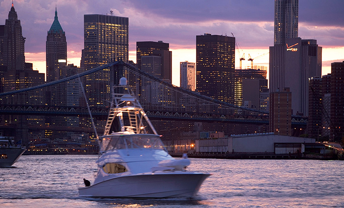 White vessel navigating waters with a city skyline in the background at sunset. 
