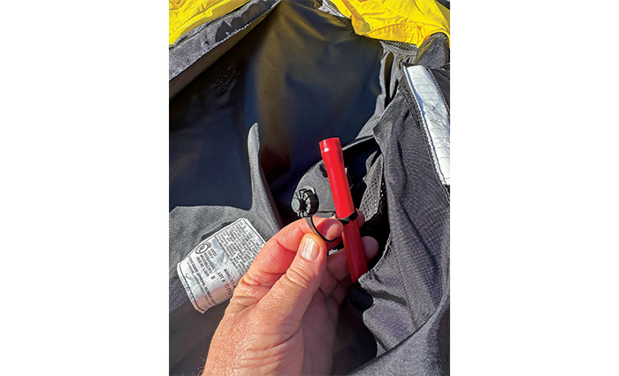 Adult hand holding a red inflatable cap on a black life jacket.