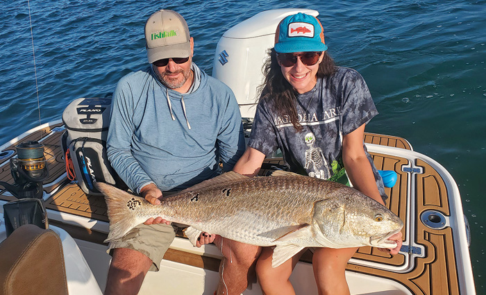 Middle aged male and female sitting on the back of a vessel proudly displaying a large fish.