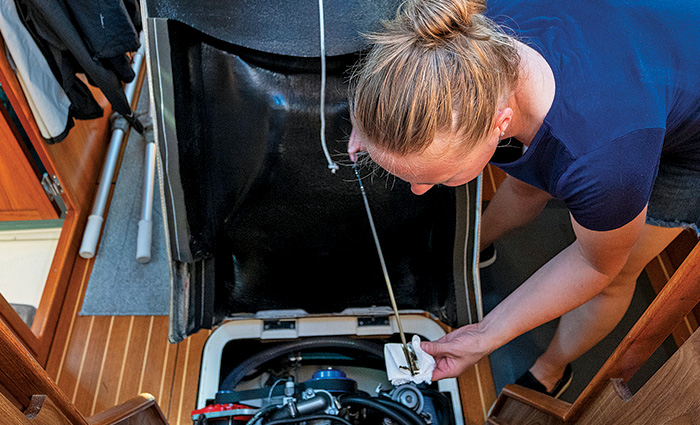 Blonde female with hair up in a bun wearing a navy shirt and jean shorts changing the oil on a vessel.