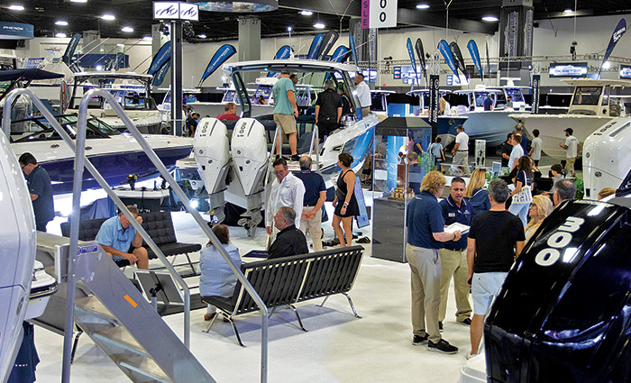 Numerous adults viewing and discussing boats inside a well lit boat show.