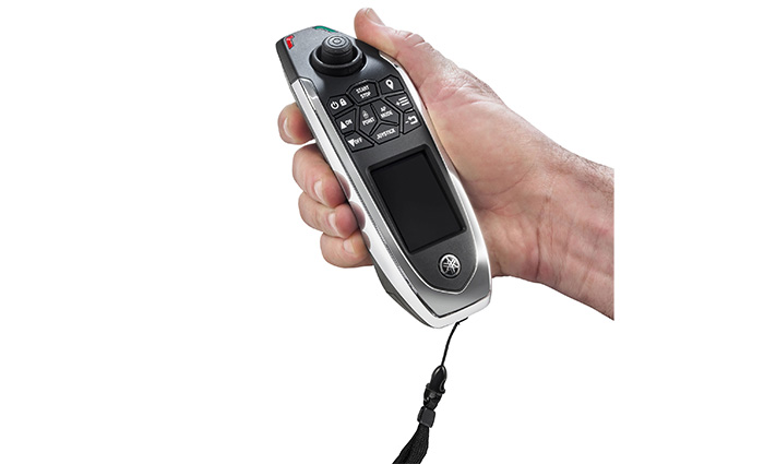 Adult hand holding a silver and black Yamaha wireless control with black joystick.