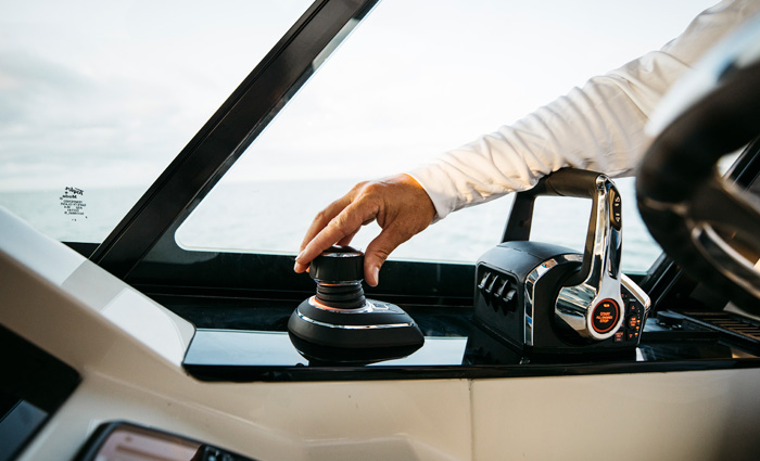 Adult wearing a white long sleeve shirt adjusting a black joystick control on a boat with open waters in the background.