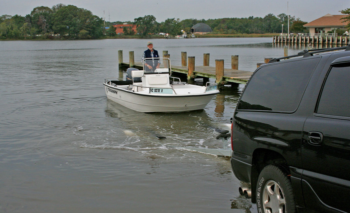 Senior adult male navigating a small white boat to a trailer next to a wooden dock.