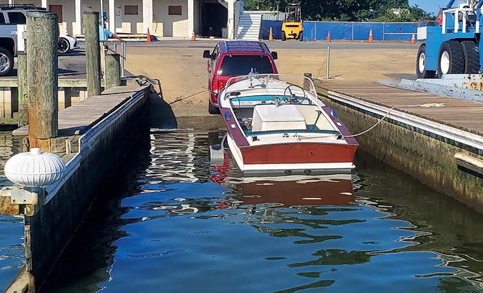 A maroon and white boat on a trailer being led into water at a marina by a red SUV.