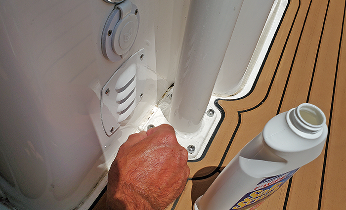 View of a male's hand next to a bottle of Soft Scrub using a cotton swab to clean caulk line of a boat deck.
