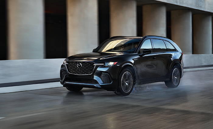 A black Mazda’s 2026 CX-70 Hybrid driving down a wet road.