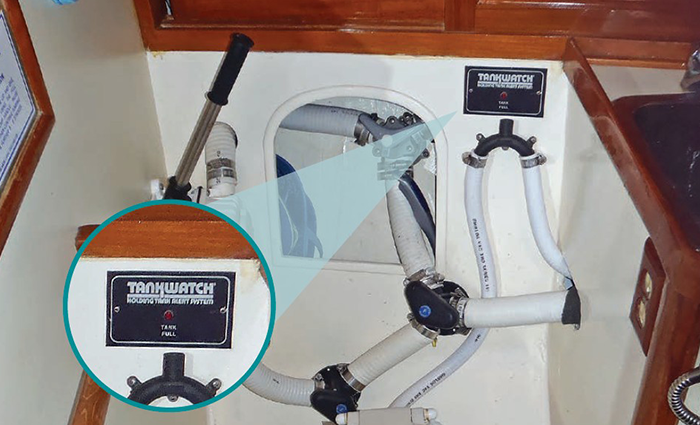 Close-up view of a black Tankwatch holding tank monitoring system next to a white toilet in a bathroom.