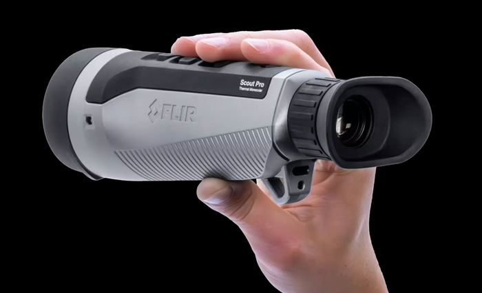 Adult hand holding a gray and black portable thermal imaging monocular.