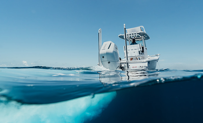 View from behind of a large white vessel with white Mercury outboard engine speeding through clear blue waters.