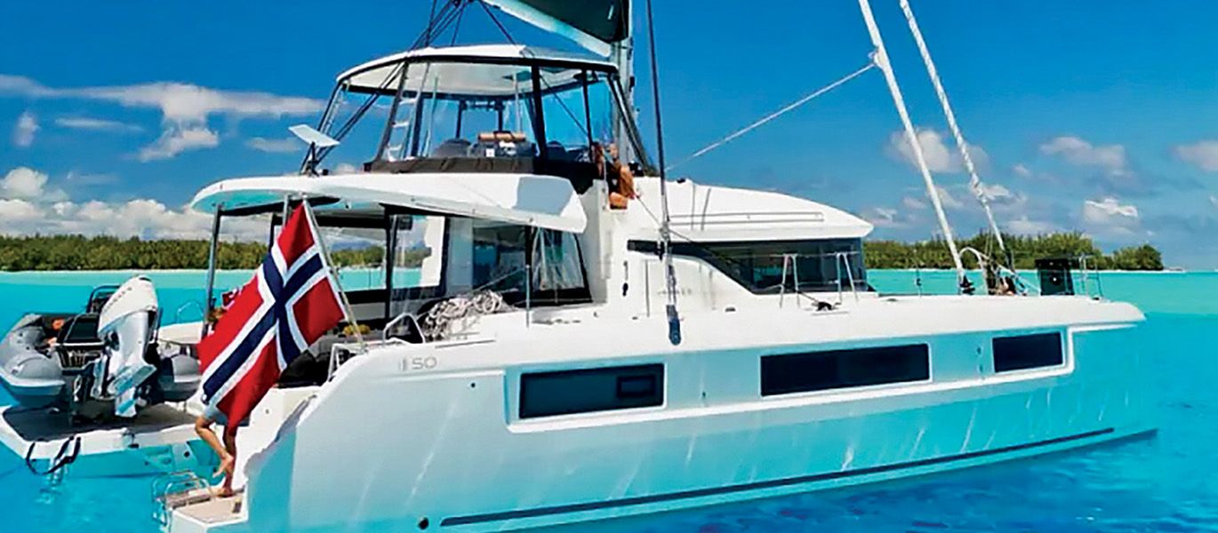 White vessel flying a Norwegian flag on clear blue waters during a sunny day.