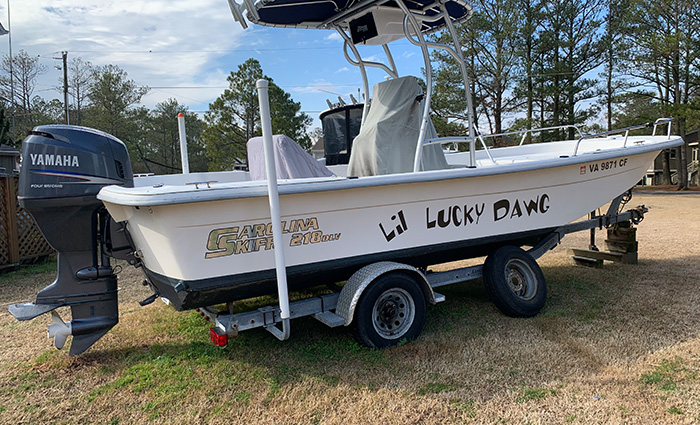 White boat on a trailer with trees and blue shy in the background.