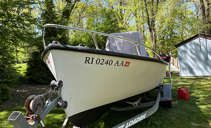 White boat with black trim and black lettering on a trailer in a backyard.